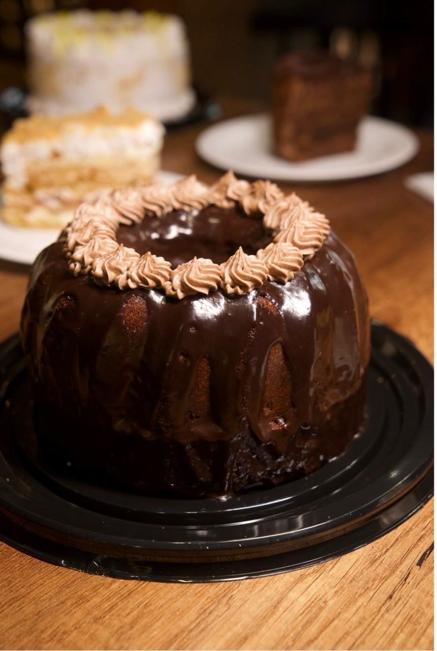 Torta cubierta de chocolate y decorada con crema sobre una mesa de madera.
