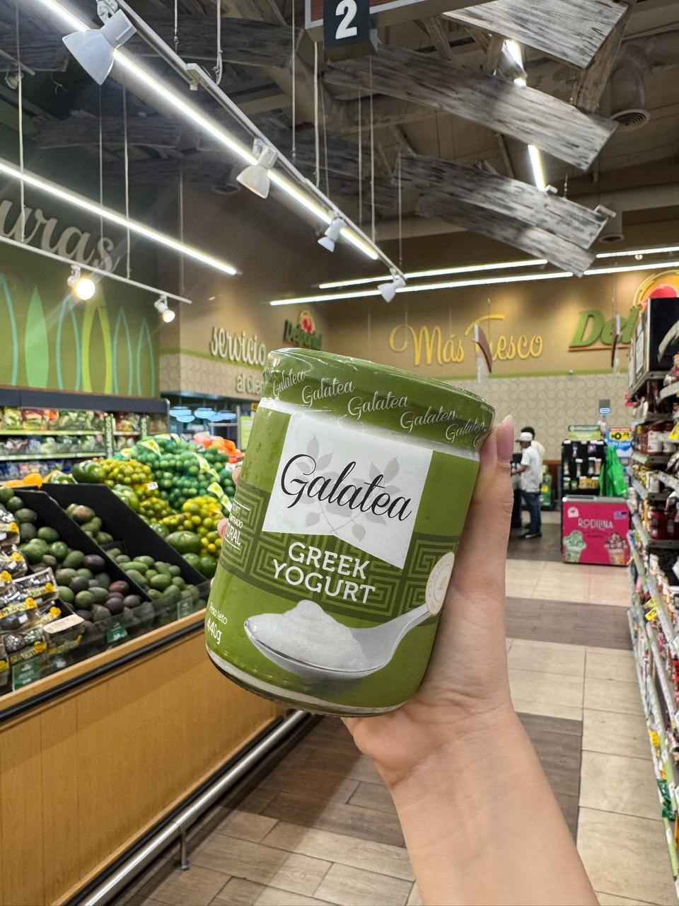 Una mano sostiene un envase de yogurt griego en un supermercado.