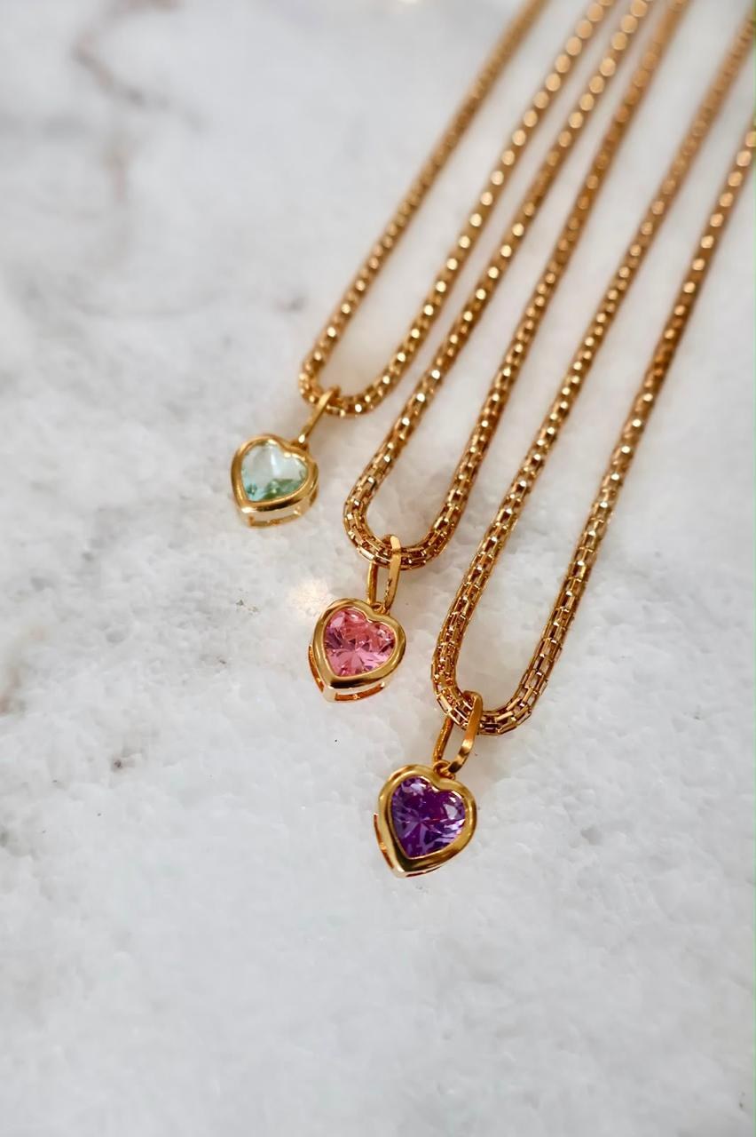 Cuatro collares dorados con colgantes de piedras de colores sobre mármol blanco.