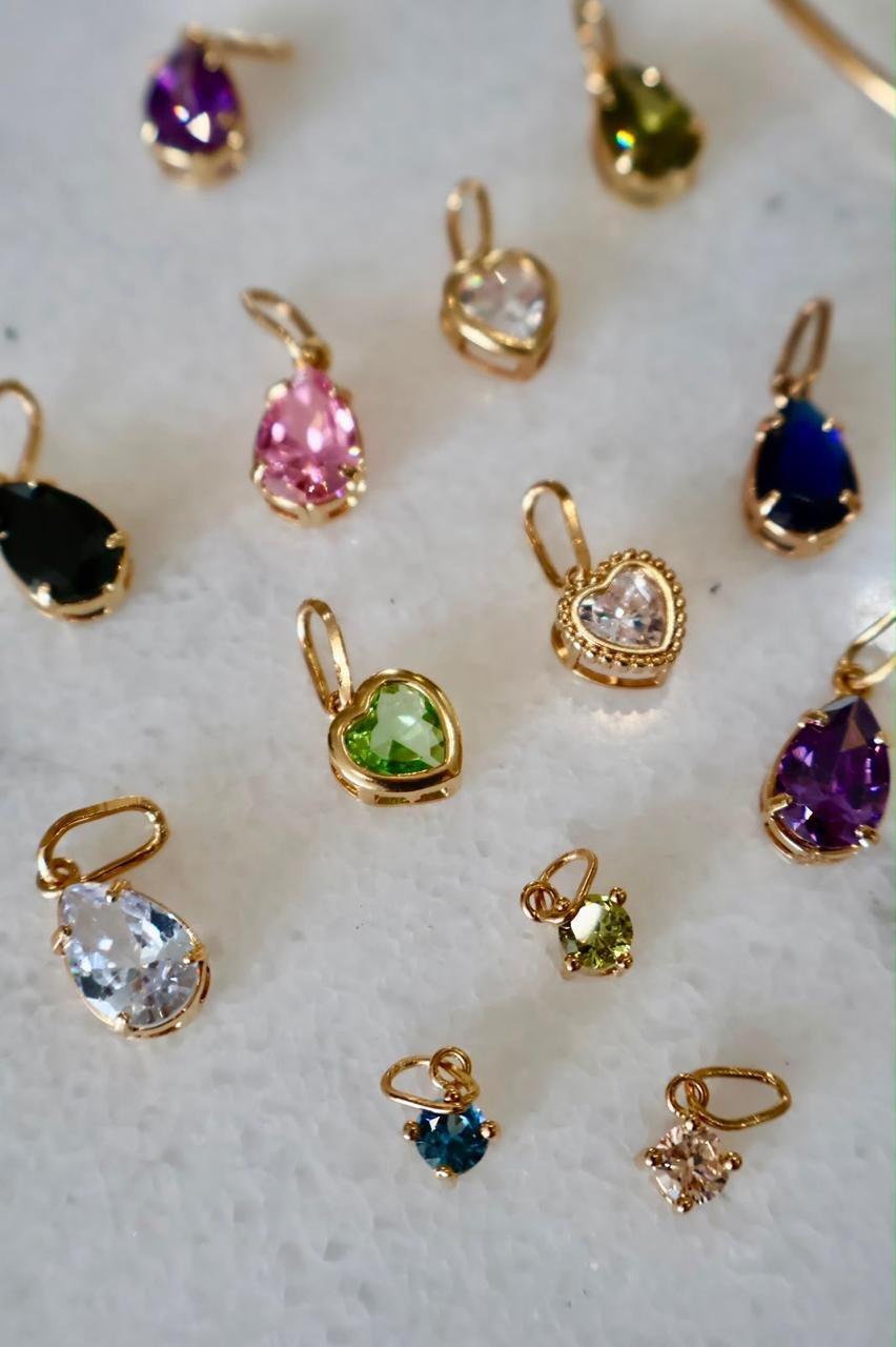 Dijes dorados con piedras de distintos colores distribuidos sobre una superficie clara.